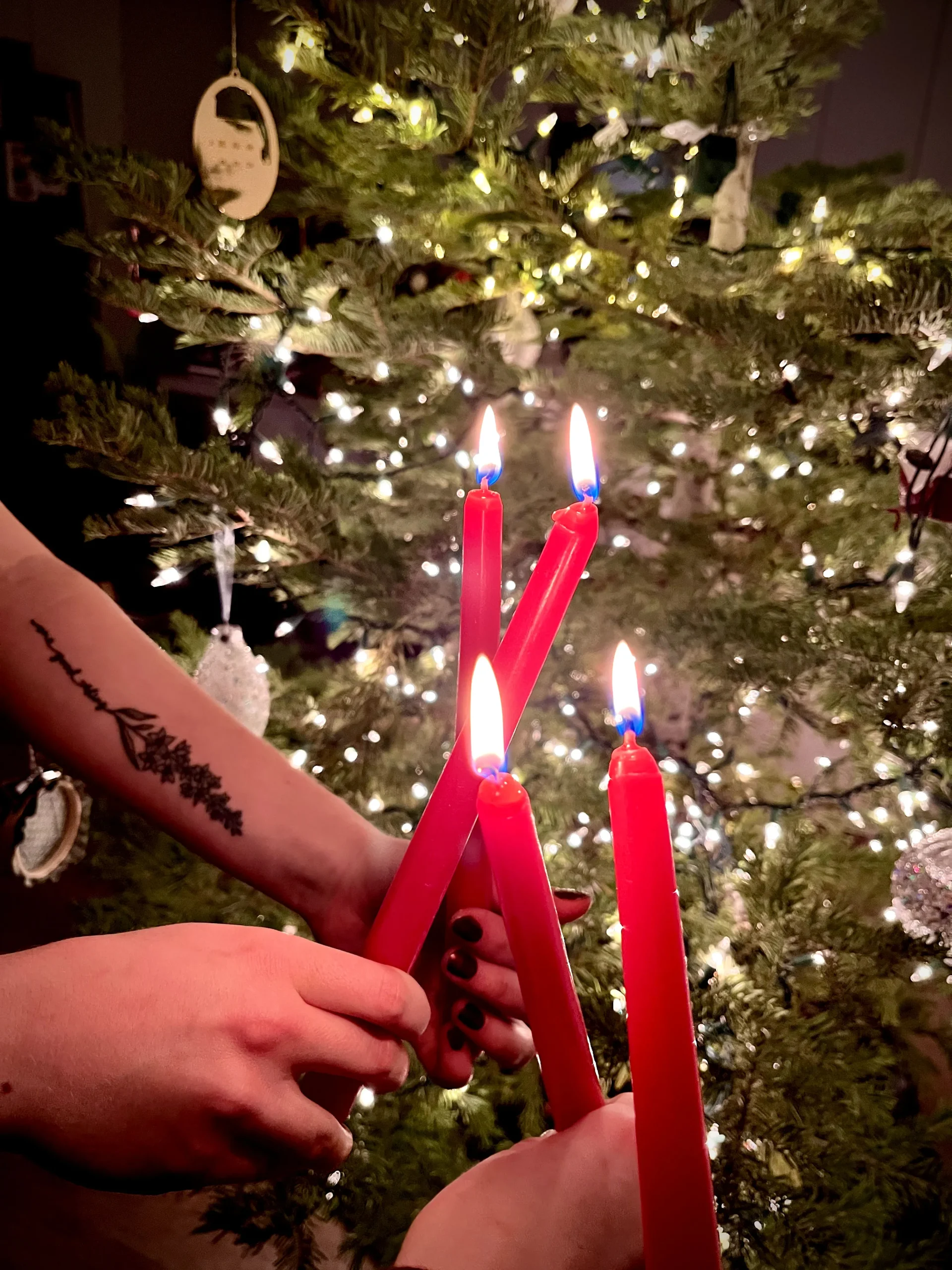 Hands passing the flame between red candles in front of a Christmas tree