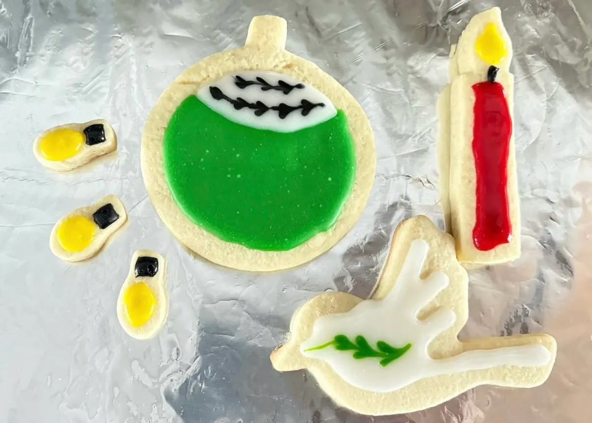 Christmas cookies decorated with a red candle, a dove, and lights