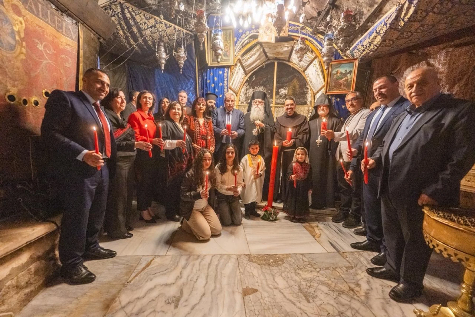 Clergy and families gathered with red candles in the Grotto of the Church of the Nativity