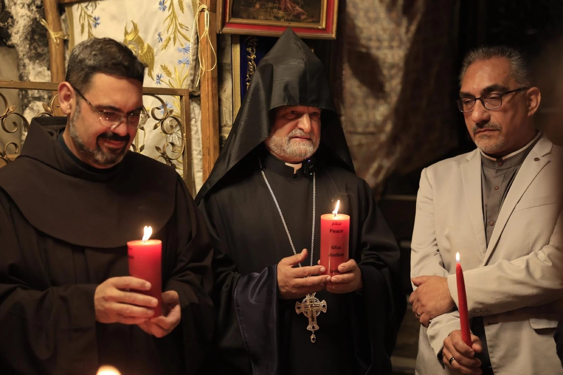 Three heads of churches holding red candles in the Grotto of the Church of the Nativity
